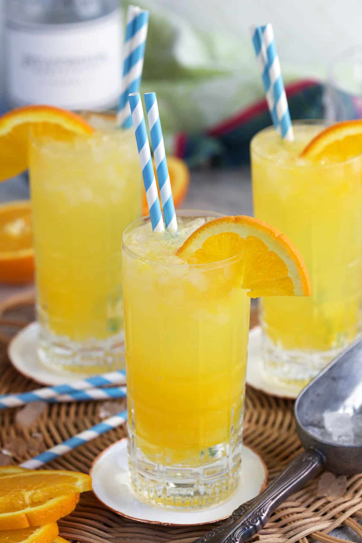 Orange Crush Cocktail in a collins glass with an orange wedge on the side and blue and white striped straws.