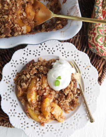 A scoop of vanilla ice cream is placed on top of the peach crisp.