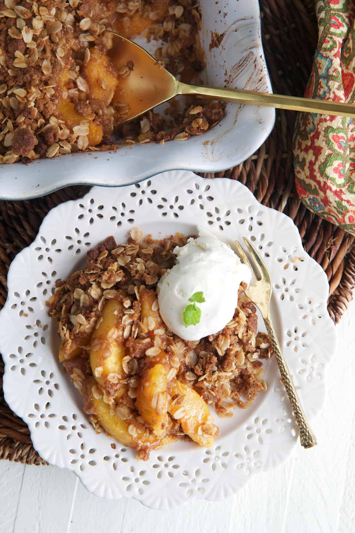 A scoop of vanilla ice cream is placed on top of the peach crisp. 