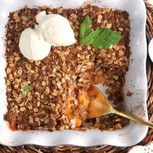 Two scoops of ice cream are placed on top of a peach crisp.