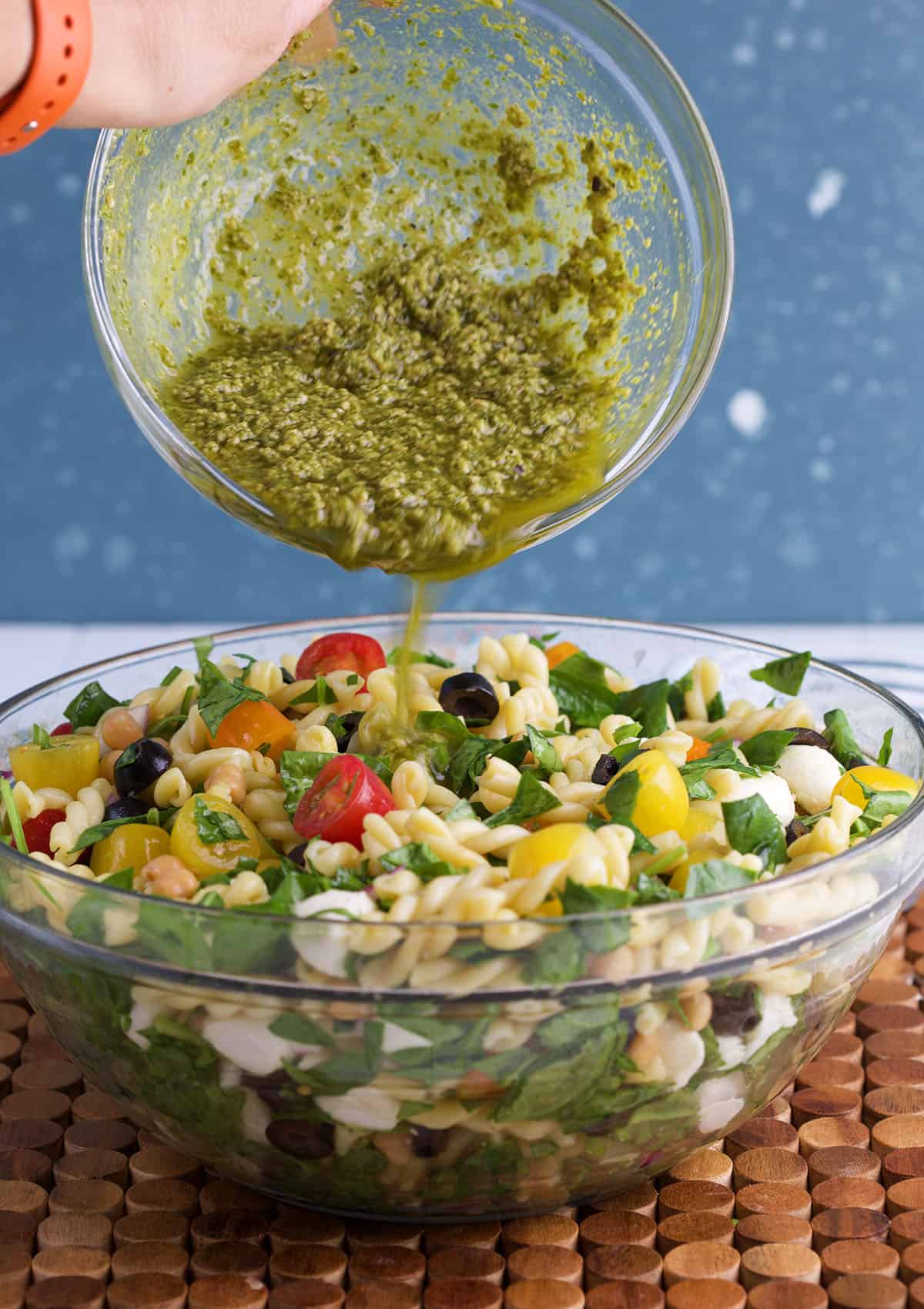 Pesto dressing is being poured over the pasta salad. 