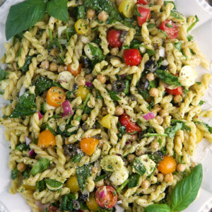 A large white platter is topped with pesto pasta salad.