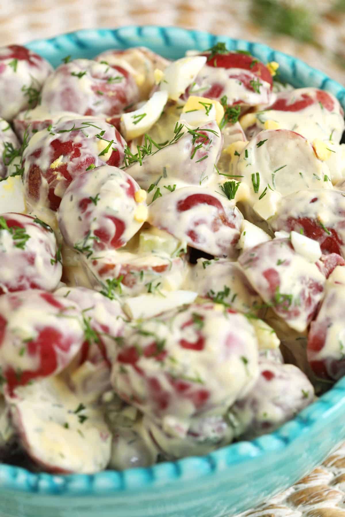 A bowl of red potato salad is garnished with some fresh herbs. 