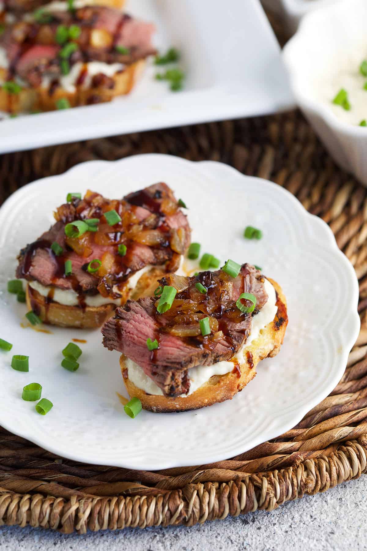 Two pieces of steak crostini are placed on a white plate. 