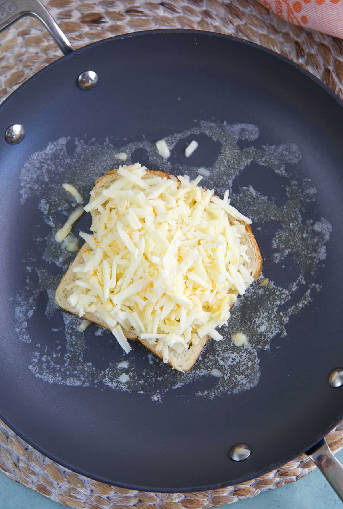 Cheese is piled on top of a slice of bread. 