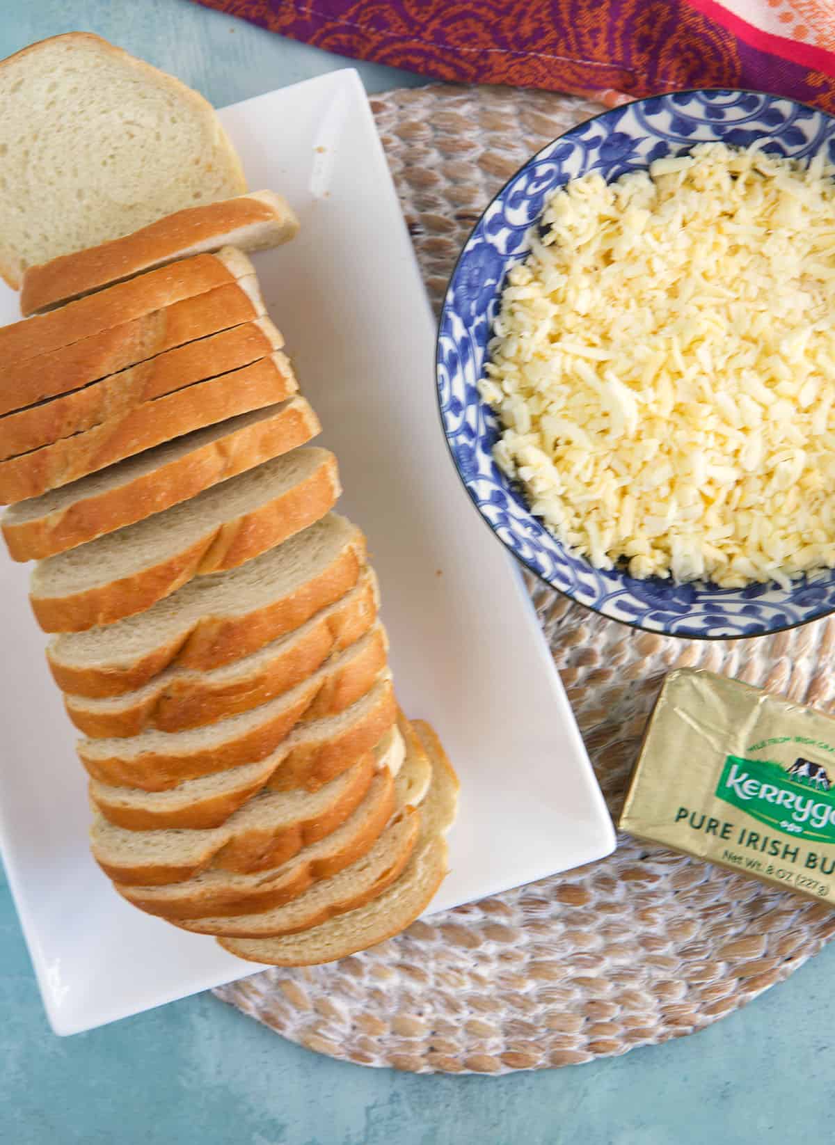 Sliced bread is placed next to a bowl of cheese and a block of butter. 