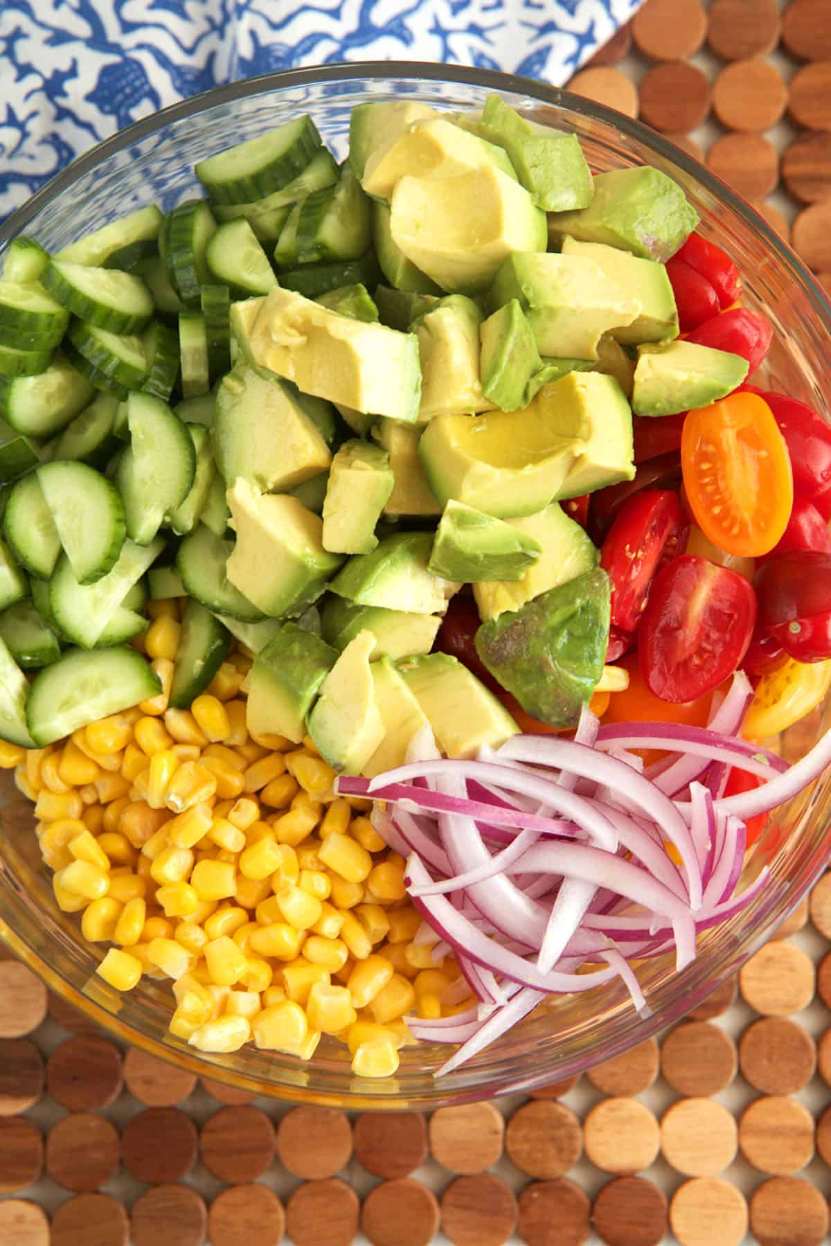 Overhead view of ingredients for avocado corn salad in glass mixing bowl before tossing