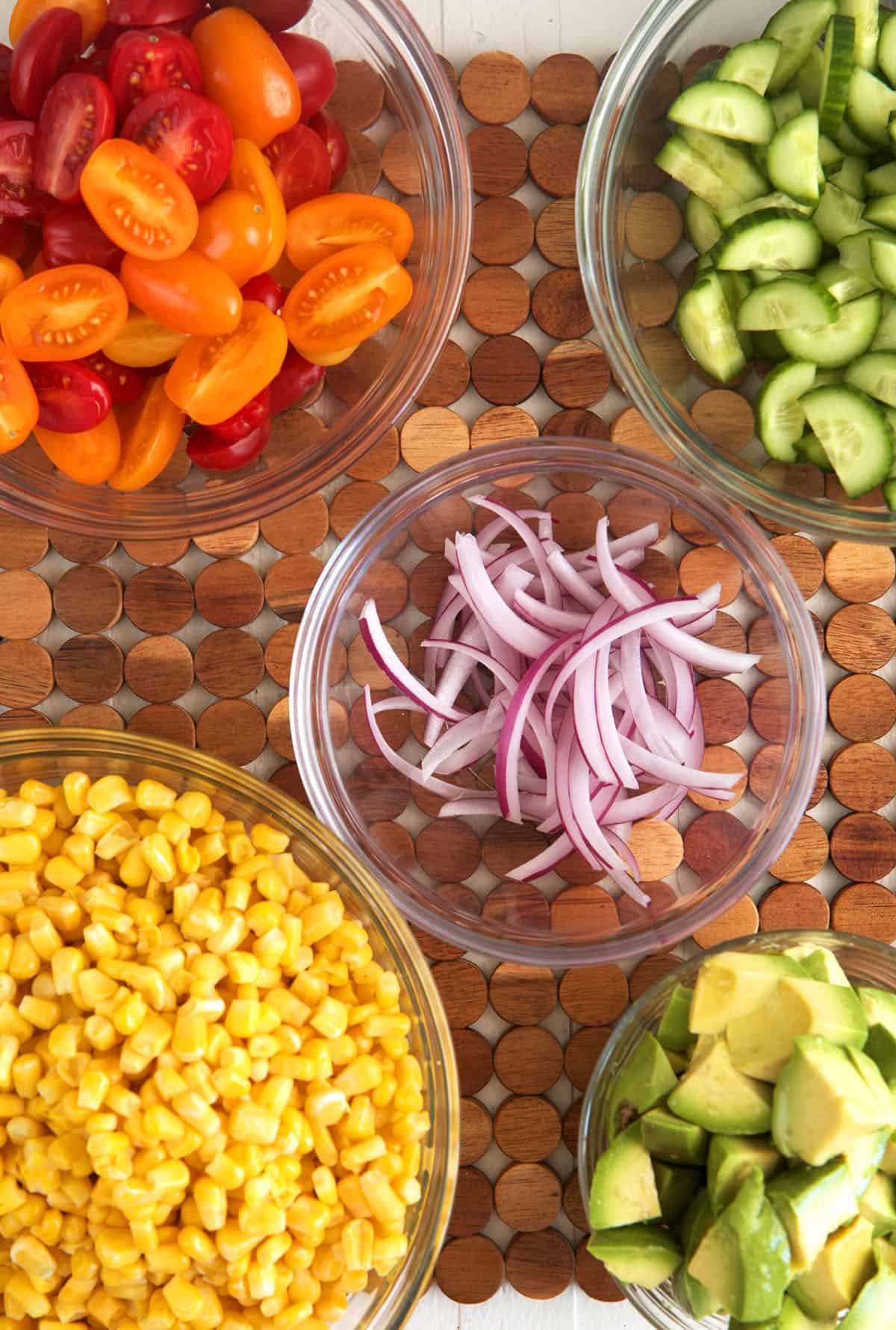 Overhead view of ingredients for avocado corn salad in glass bowls