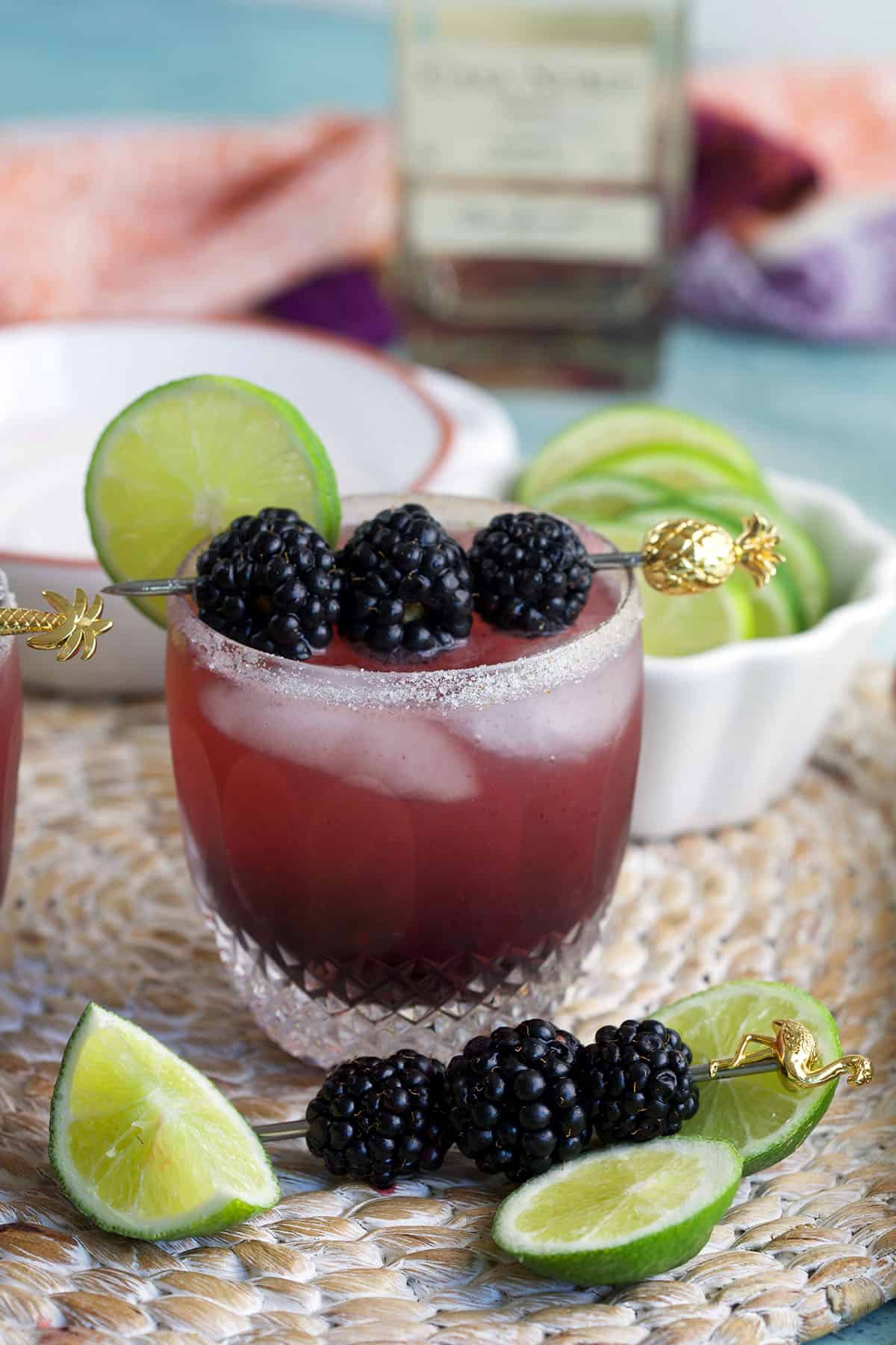 Blackberry margarita in glass with ice, fresh berries, and lime wheel for garnish