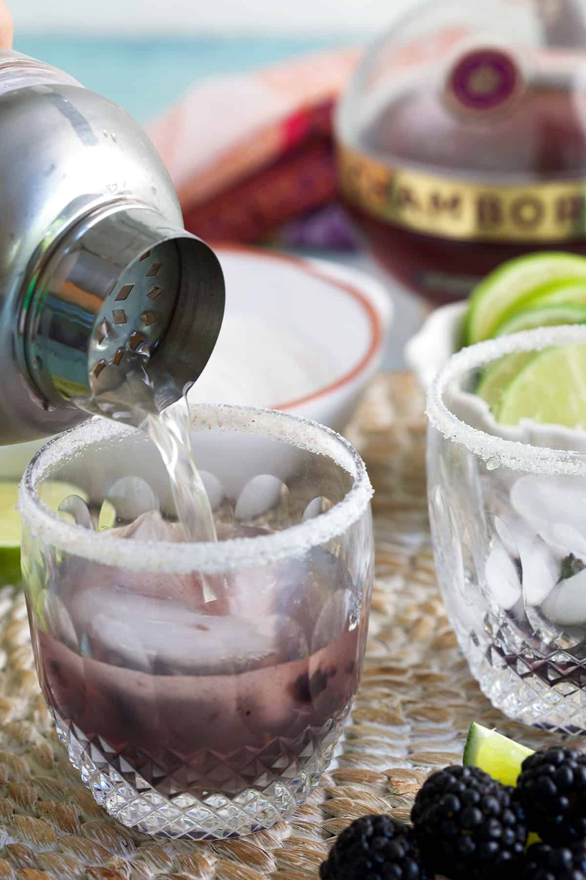 Pouring blackberry margarita over ice in rimmed glass