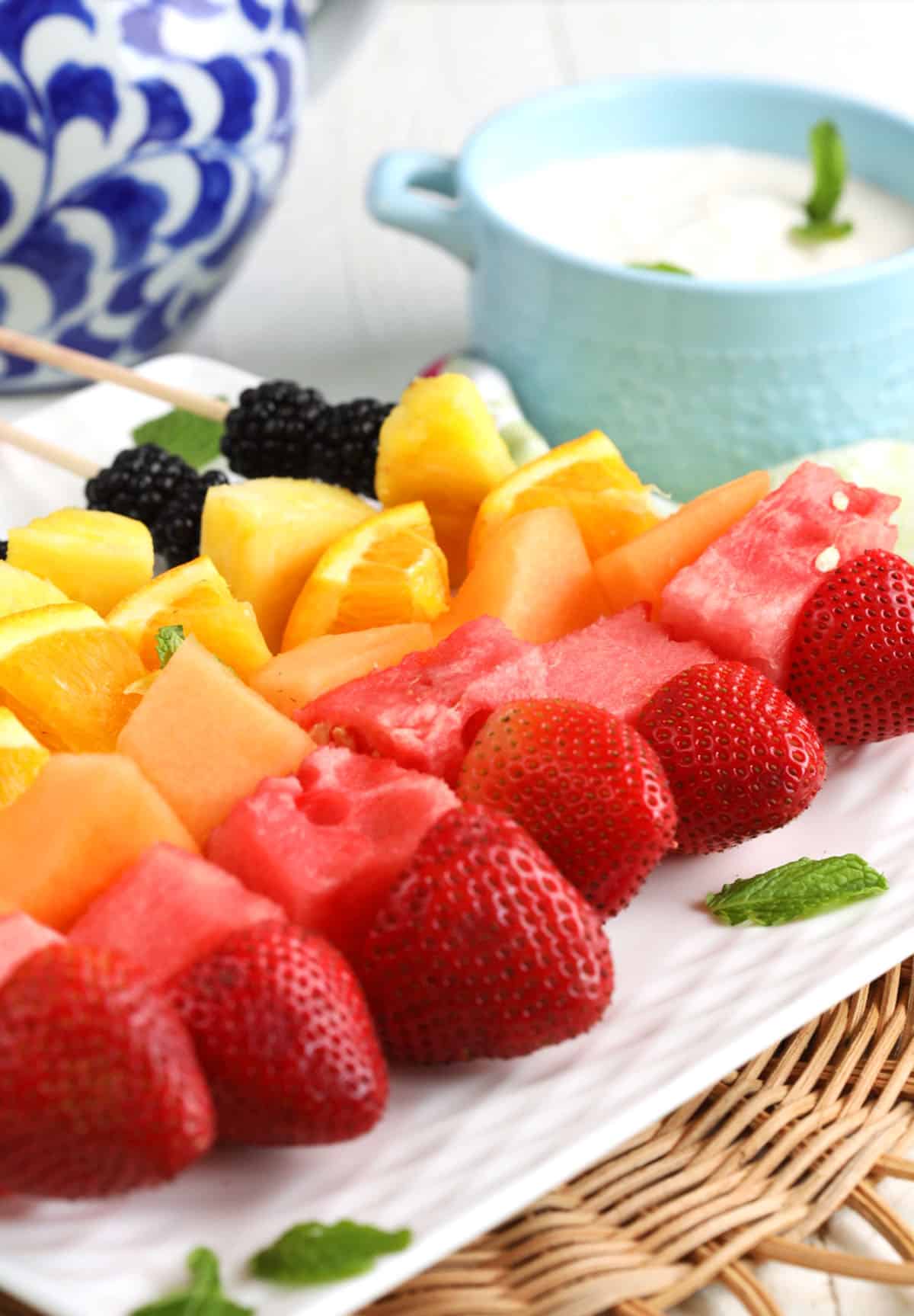 Platter of rainbow fruit kabobs with Greek yogurt dip in background