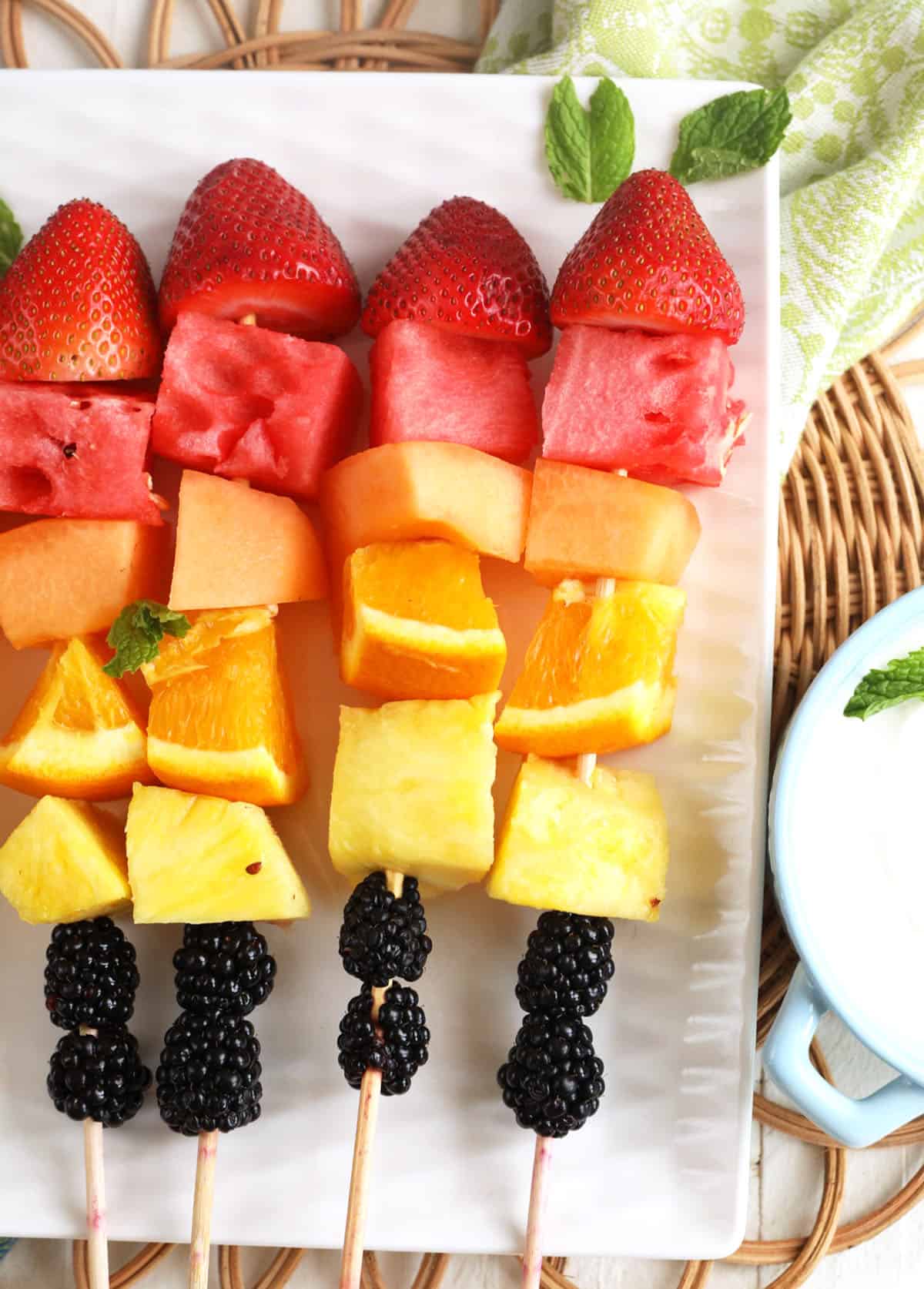 Overhead view of rainbow fruit kabobs on platter