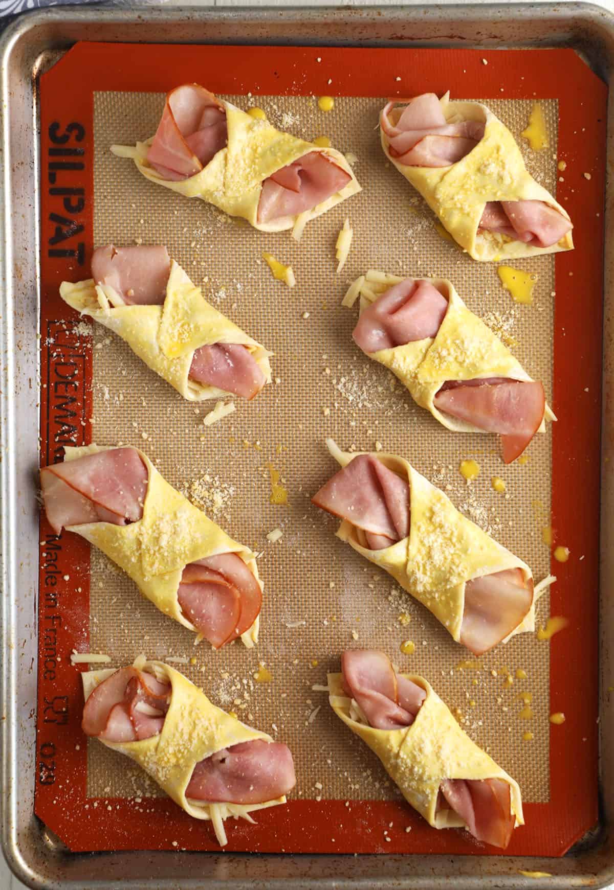 Overhead view of ham and cheese croissants on silpat-lined baking sheet before baking