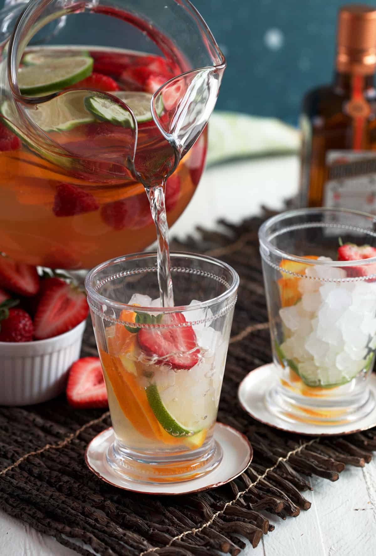 Pouring rosé sangria from pitcher into glass with fresh fruit