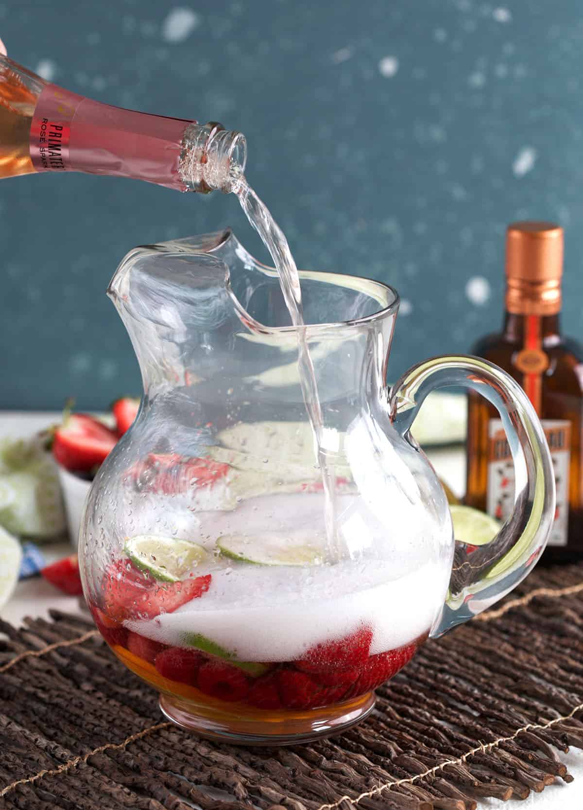 Pouring rosé into pitcher of fruit for sangria