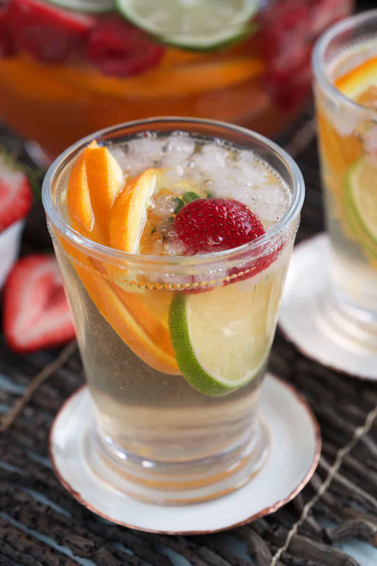 Rosé sangria in glass with ice, lime and orange slices, and strawberry