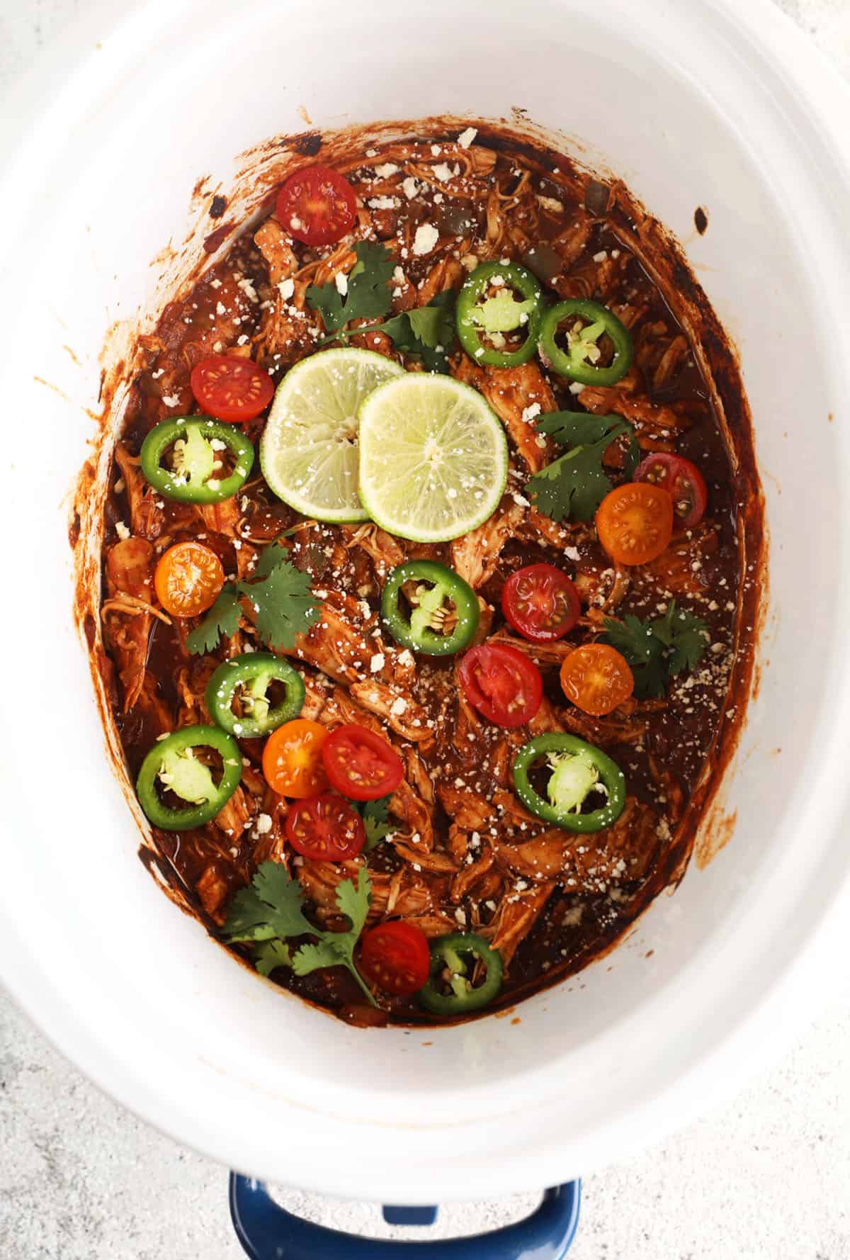 Overhead view of crockpot salsa chicken in slow cooker insert with garnishes