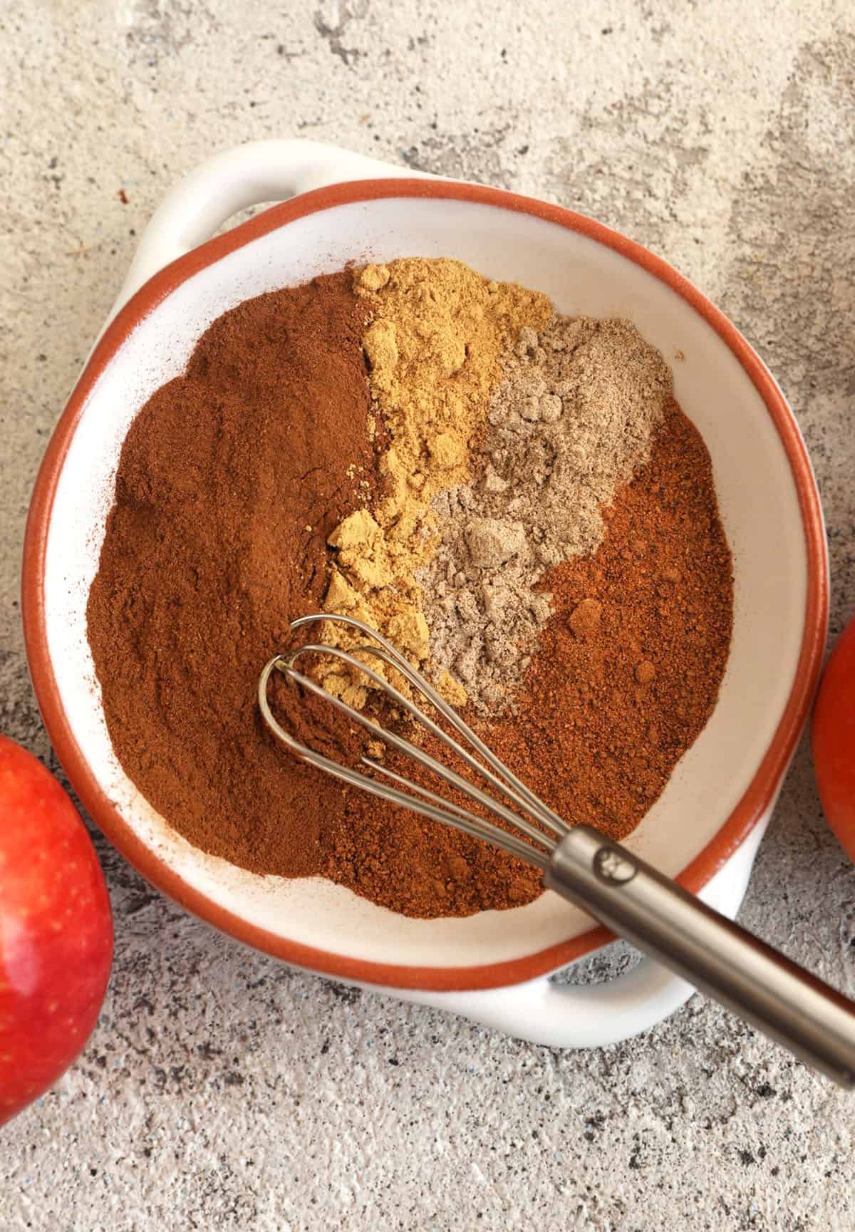 Overhead view of ingredients for apple pie spice in bowl with whisk