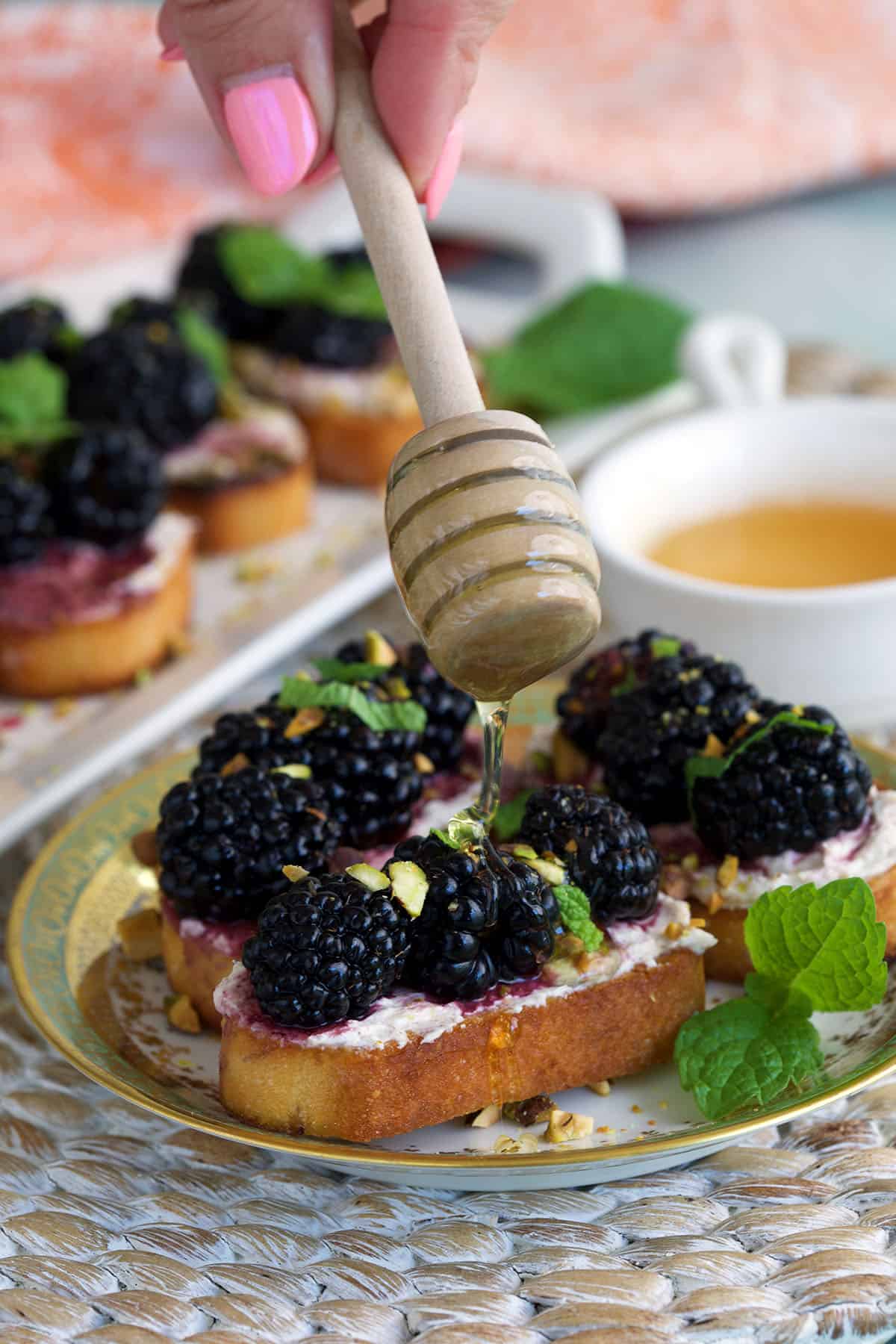 Drizzling honey onto blackberry goat cheese crostini