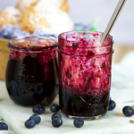 two jars of blueberry jam on a white marble board.