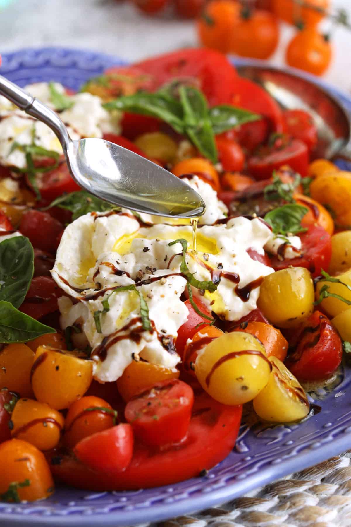 Drizzling olive oil onto burrata caprese salad