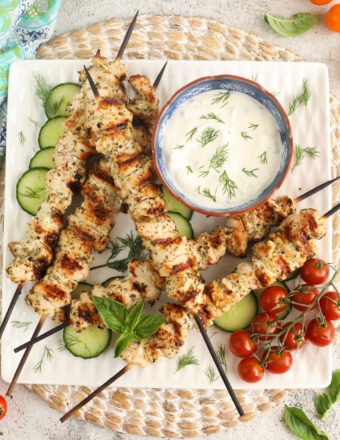 Overhead view of chicken souvlaki on platter with tzatziki, cucumbers, and cherry tomatoes