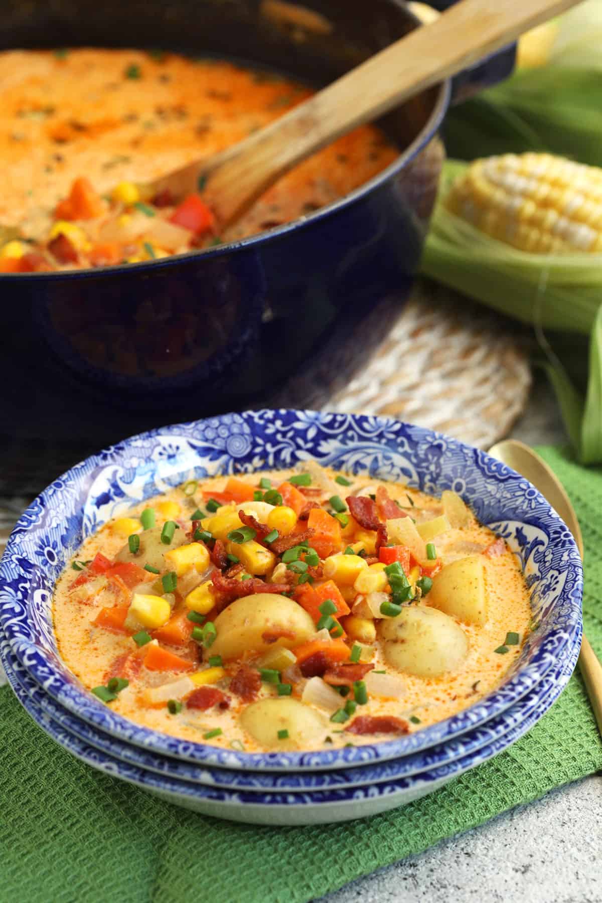 Bowl of corn chowder in bowl set next to Dutch oven