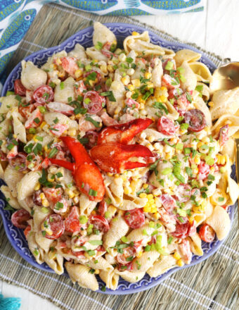 Lobster pasta salad in a large blue serving bowl with two lobster claws on top of the salad.