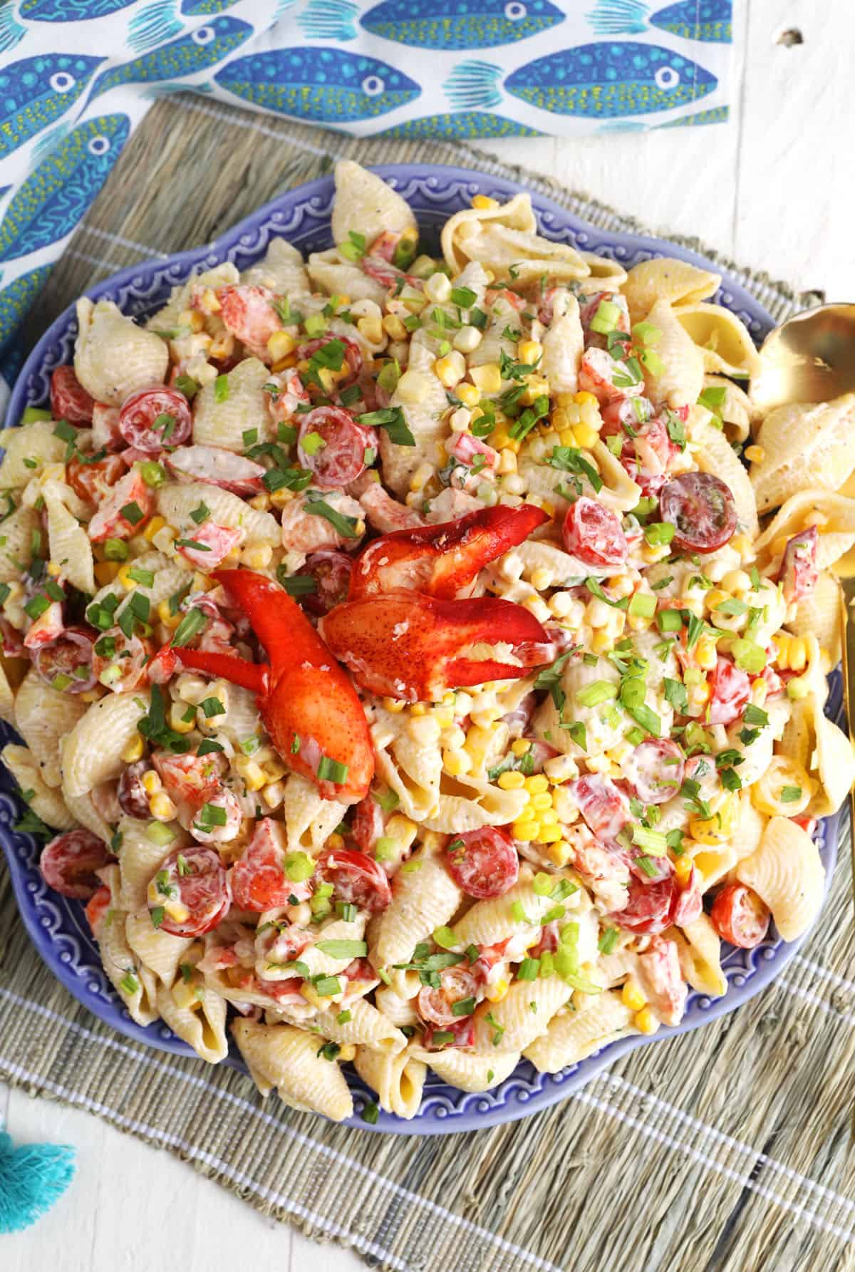 Lobster pasta salad in a large blue serving bowl with two lobster claws on top of the salad.