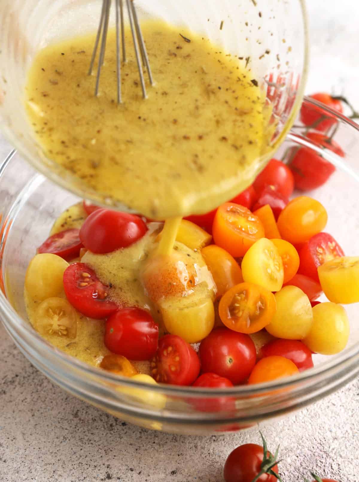 Pouring lemon dressing into bowl of multicolored cherry tomatoes