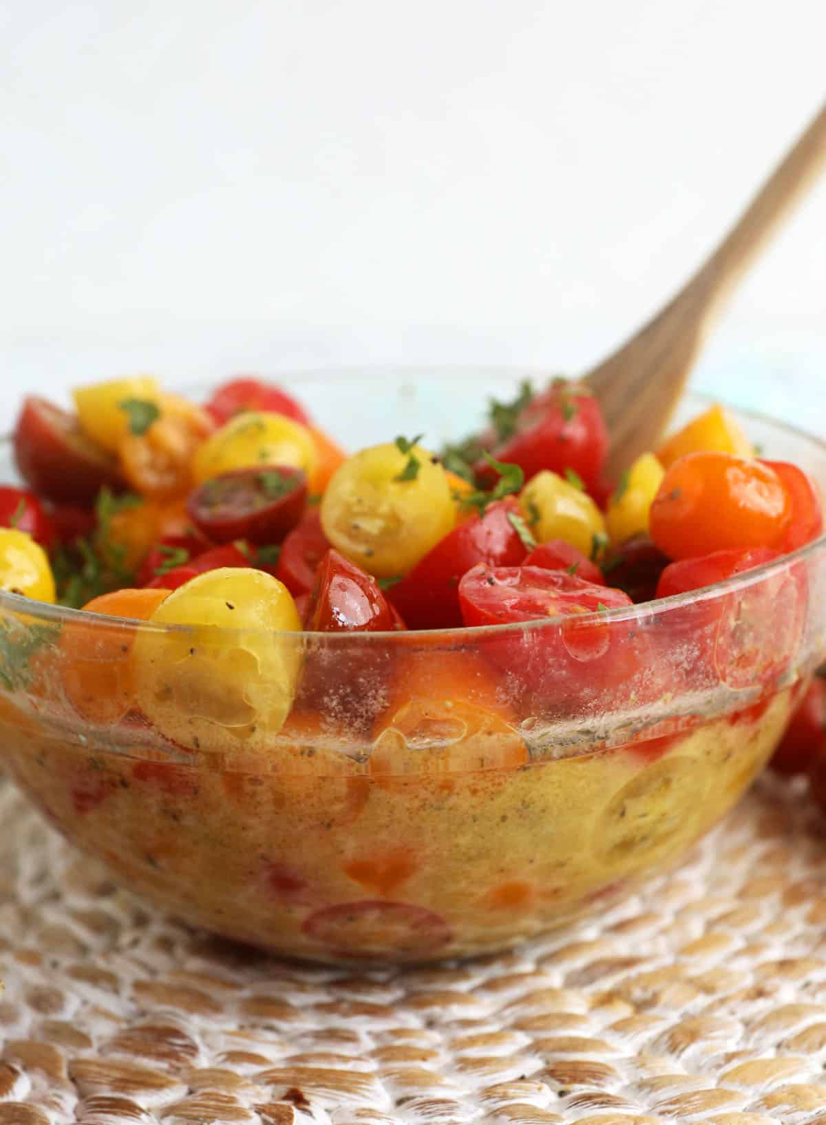 Marinated tomatoes in glass bowl with wooden spoon