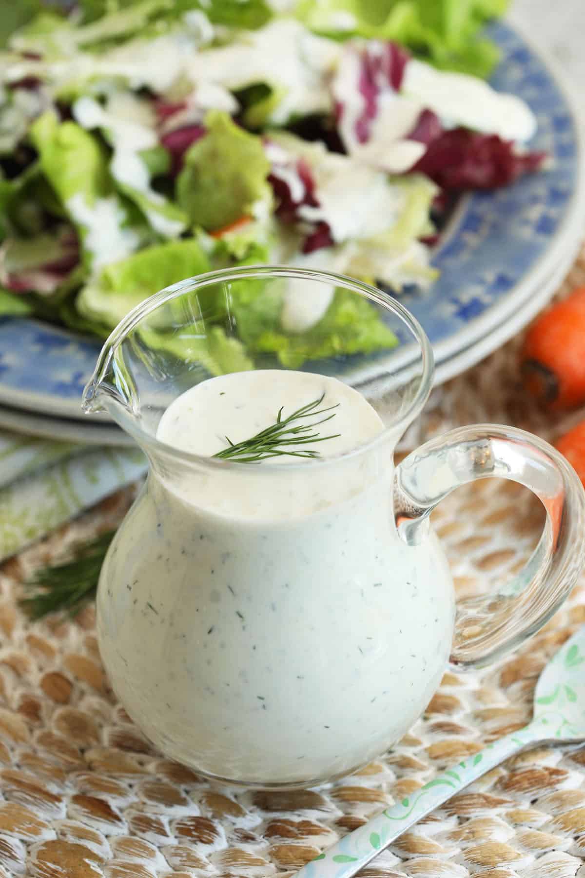 Ranch dressing in glass pitcher with salad in background