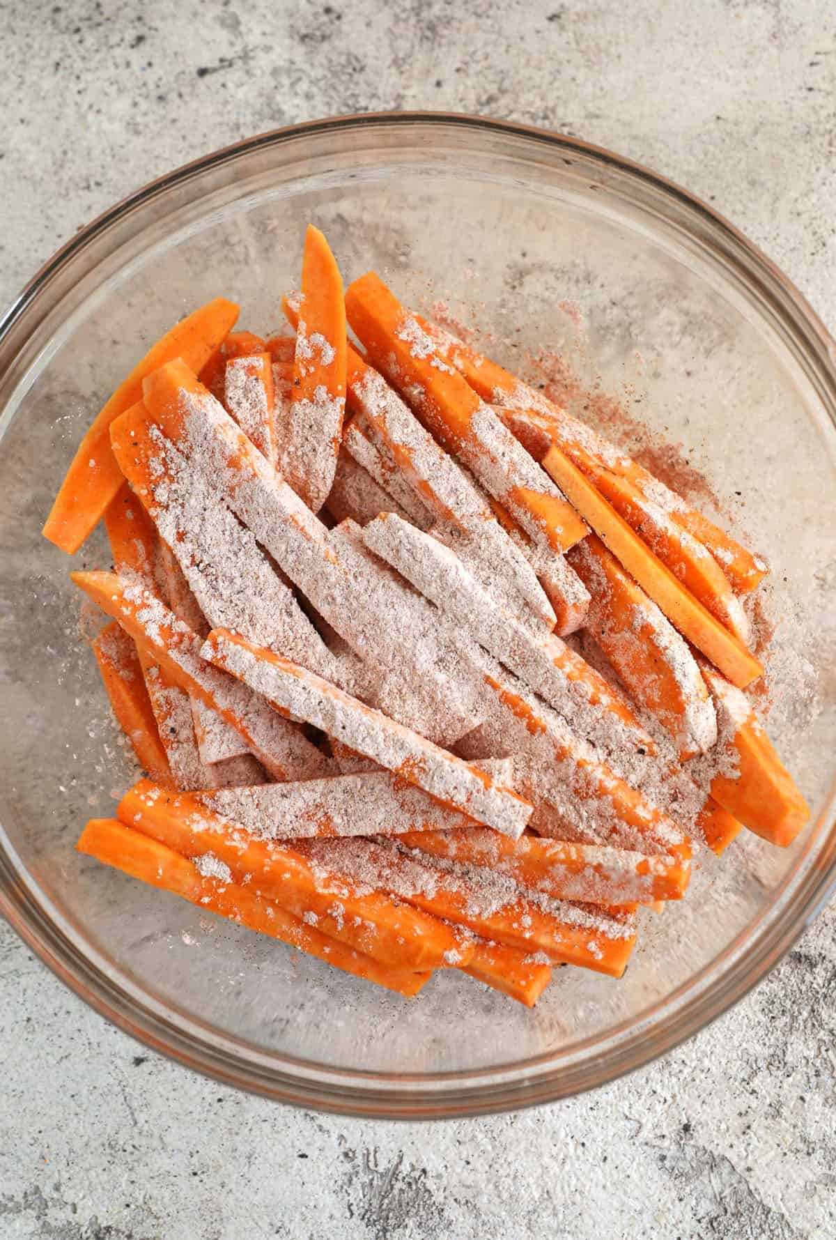 Adding seasoning to sweet potato fries in mixing bowl