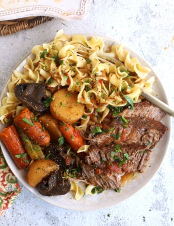 Overhead view of crock pot pot roast on plate with vegetables and egg noodles