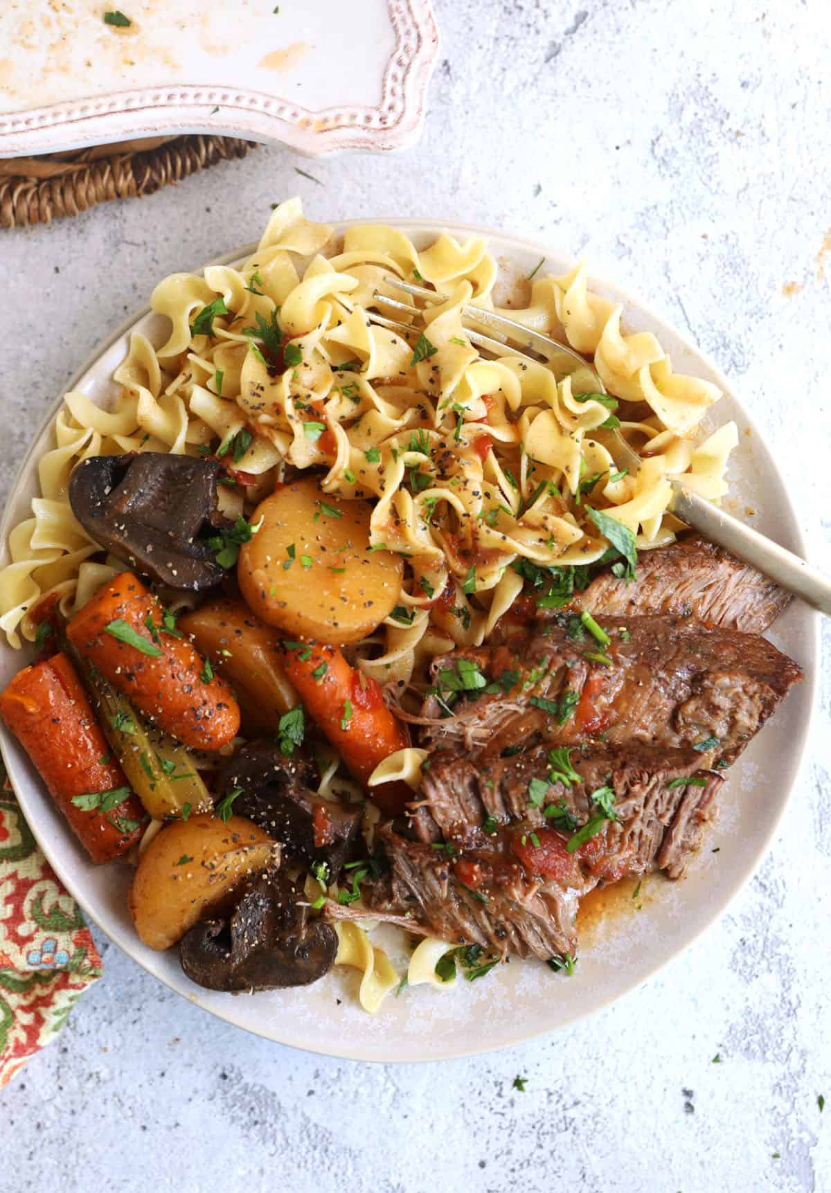 Overhead view of crock pot pot roast on plate with vegetables and egg noodles