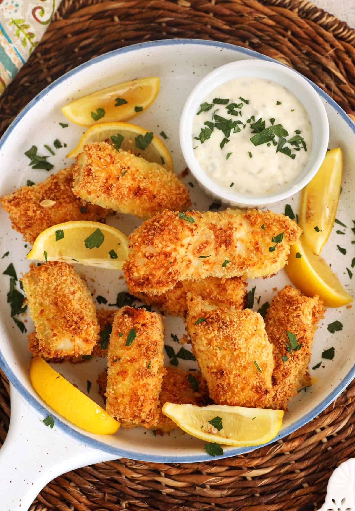 Overhead view of homemade fish sticks on plate with tartar sauce and lemon wedges