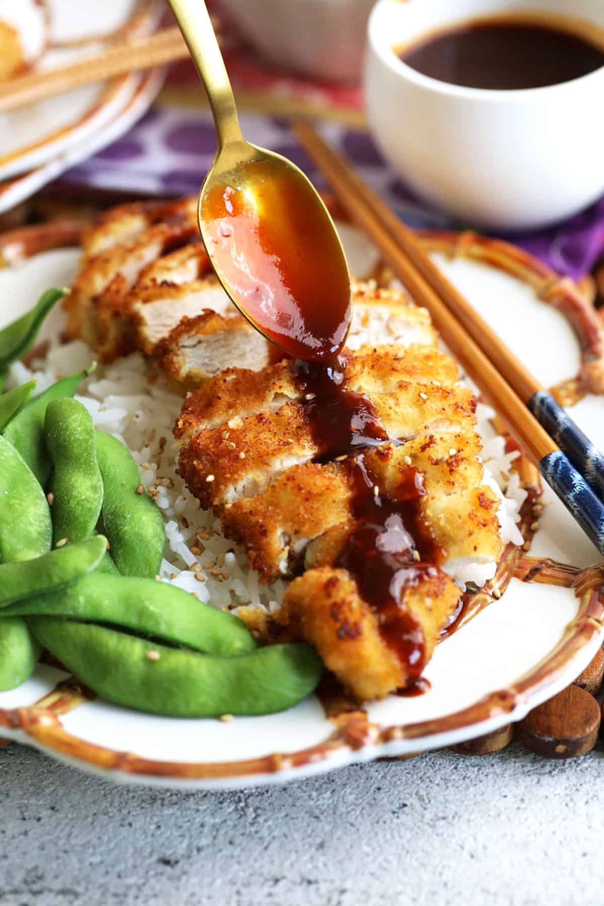 Drizzling tonkatsu sauce on plate of katsu chicken