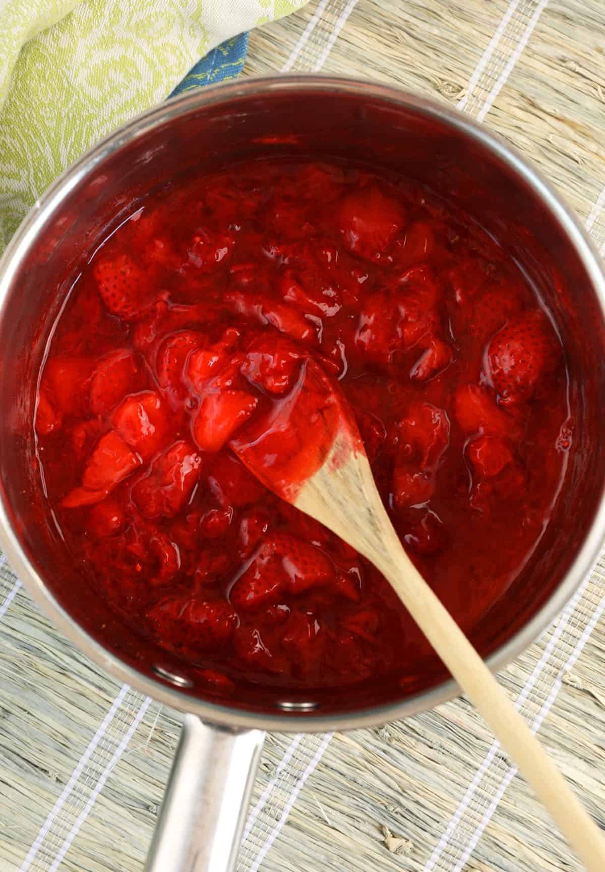 Strawberry compote in pan with wooden spoon