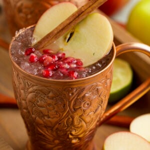 Apple cider Moscow mule in copper mug with pomegranate, apple slice, and cinnamon stick