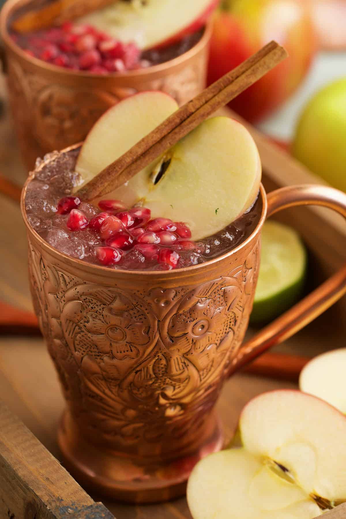 Apple cider Moscow mule in copper mug with pomegranate, apple slice, and cinnamon stick