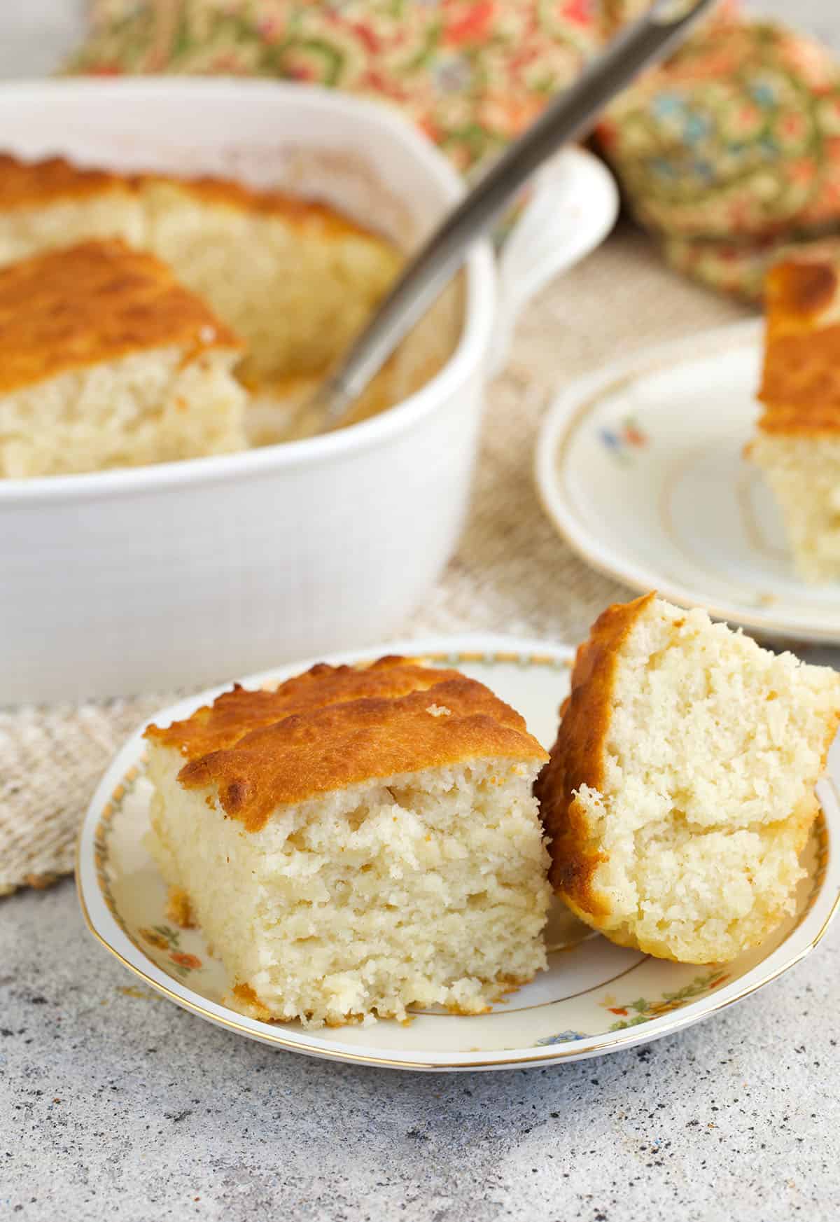 Two butter swim biscuits on plate with baking dish of biscuits in background