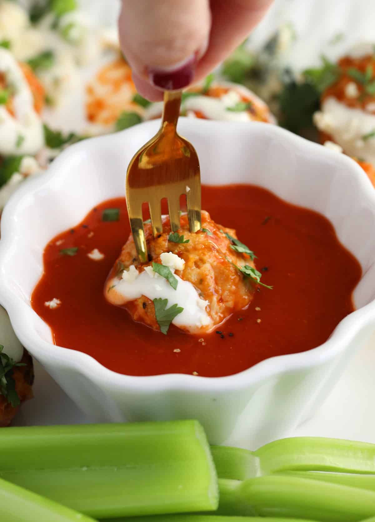 Dipping Buffalo chicken meatball in bowl of sauce