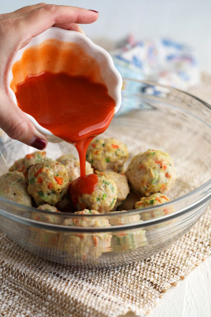 Pouring Buffalo sauce over chicken meatballs in bowl