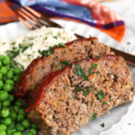 Two slices of Cracker Barrel meatloaf on plate with mashed potatoes and peas