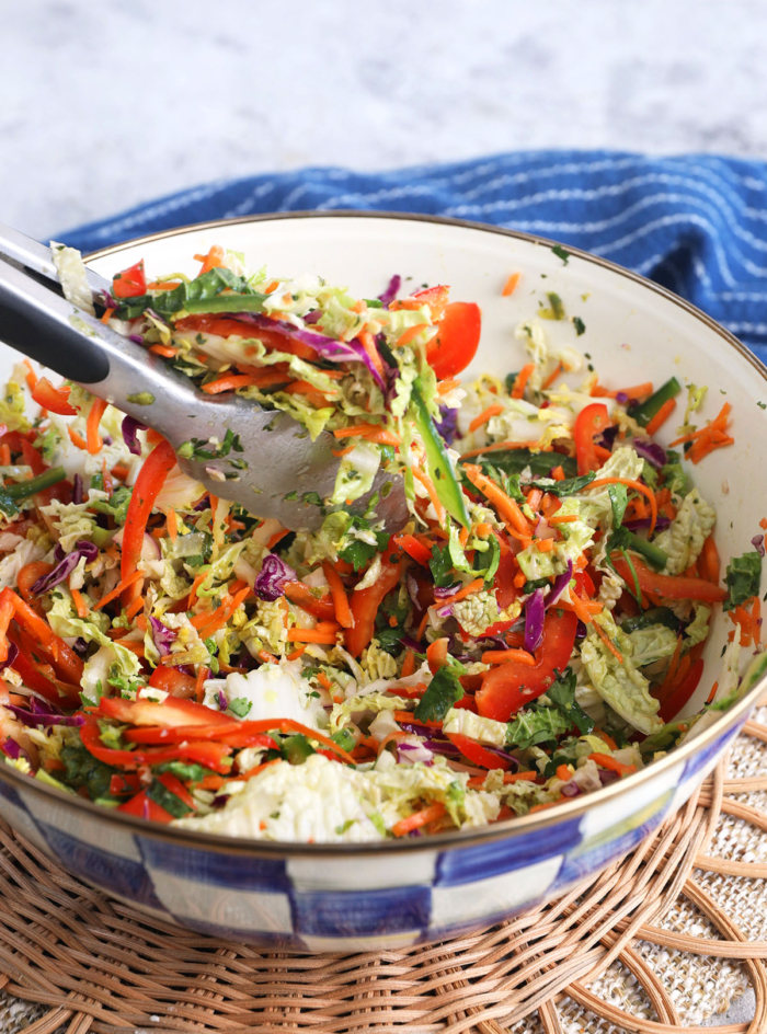 Tongs tossing Mexican coleslaw in bowl