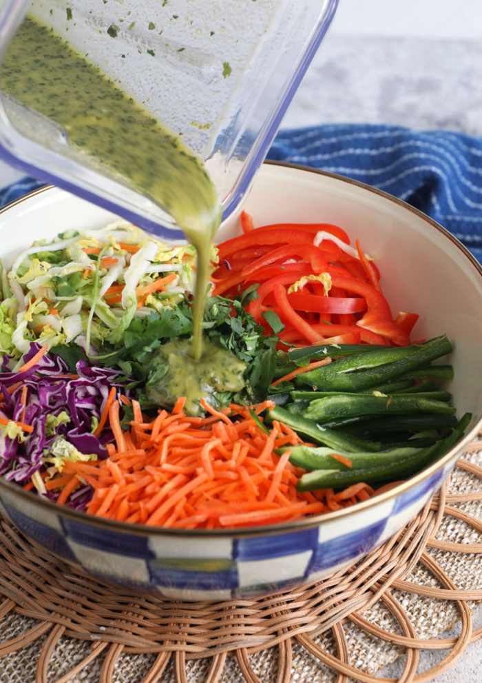 Pouring cilantro lime vinaigrette into bowl of veggies for Mexican coleslaw
