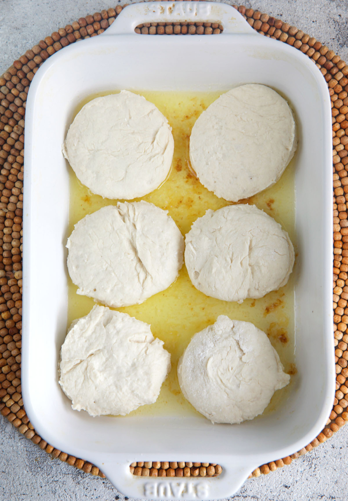 biscuits ready for baking in a white baking dish with melted butter