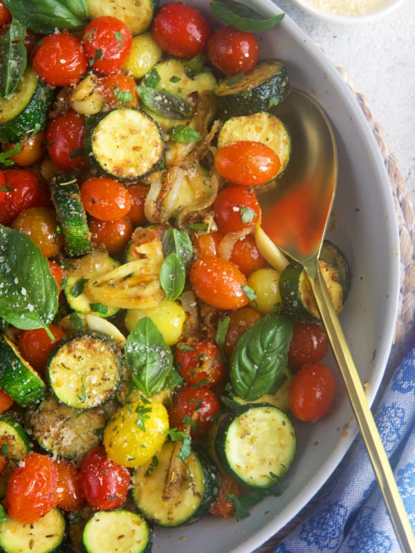 Sauteed Zucchini with tomatoes in a skillet with a gold spoon