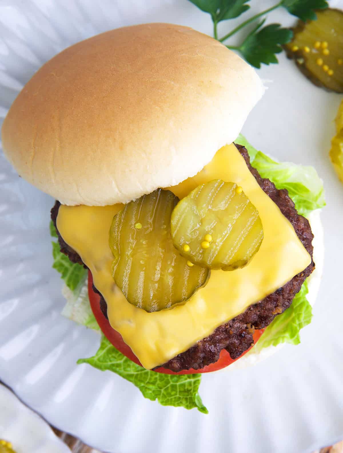 air fryer cheeseburger with pickles on top on a white plate.