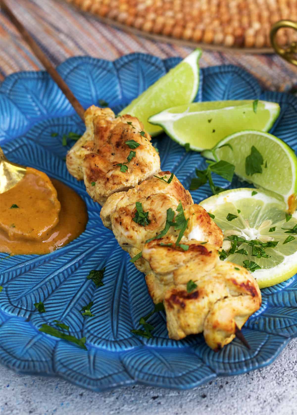 Chicken Satay on a blue plate with lime wedges and a spoonful of peanut sauce.